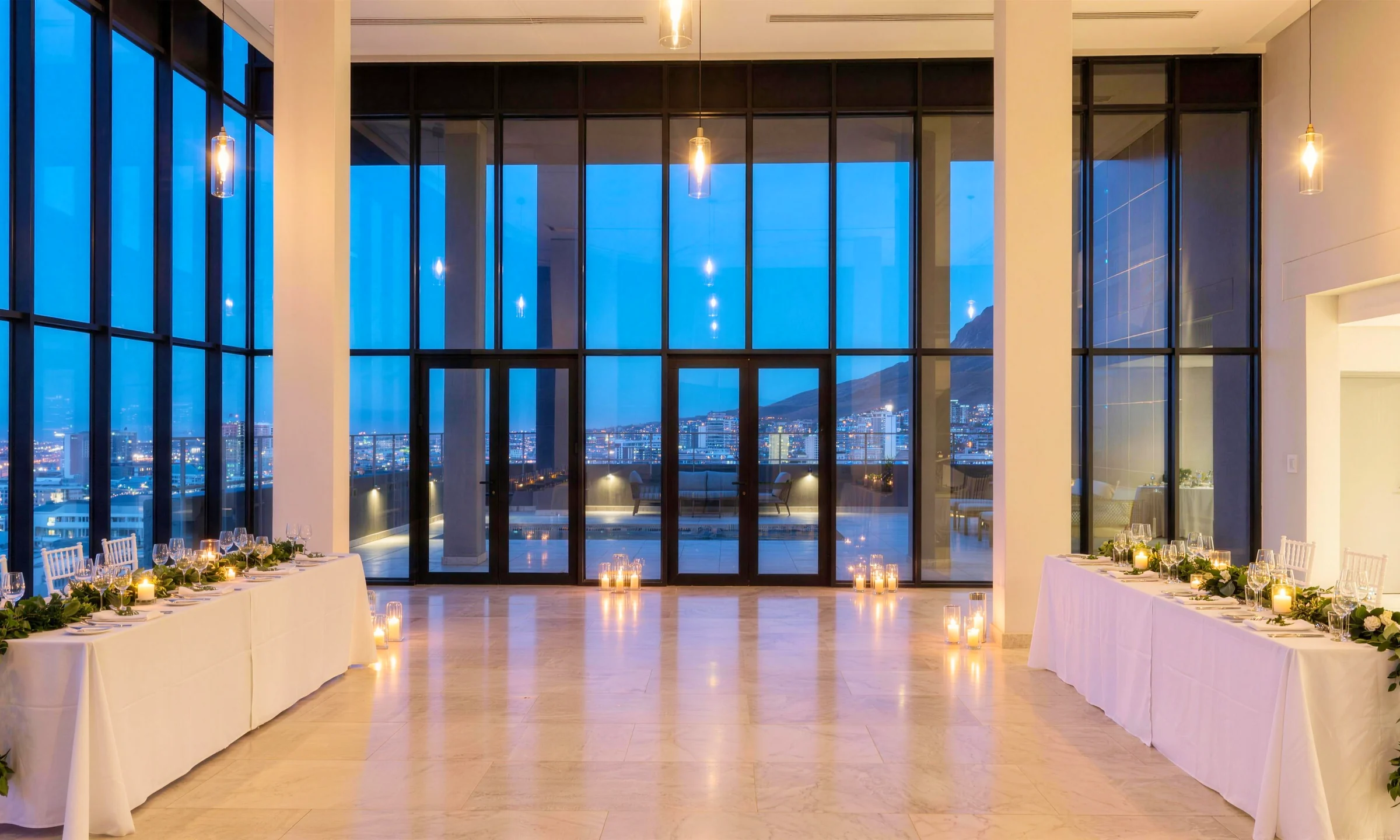 A double-height event hall set for an evening reception, candlelit tables before the glass