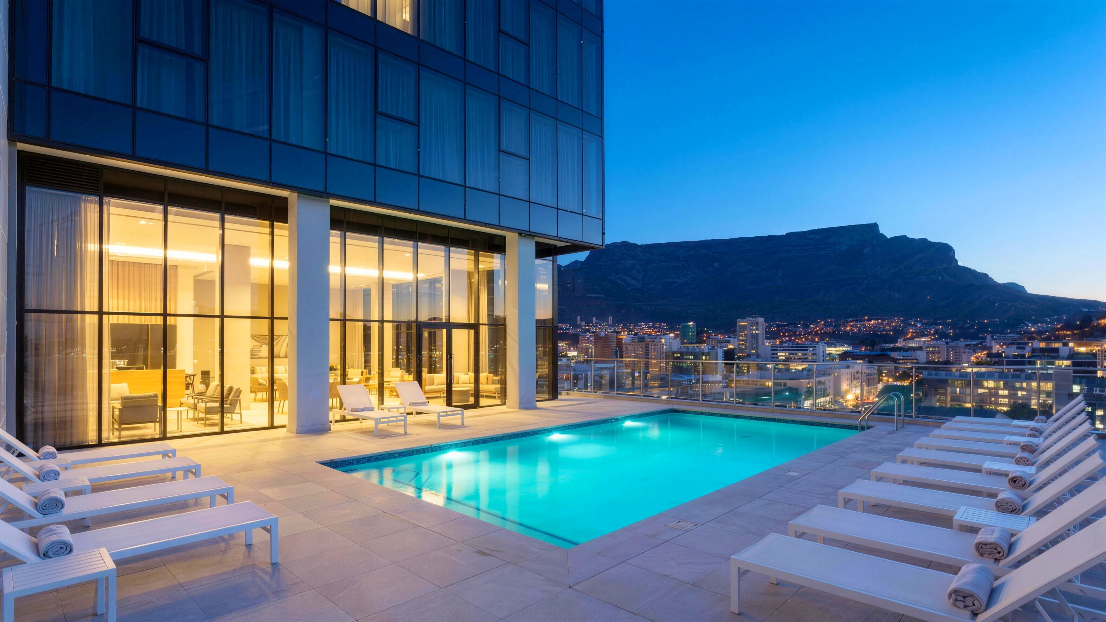 The level-22 pool deck at blue hour, the pool glowing turquoise with the city and Table Mountain beyond